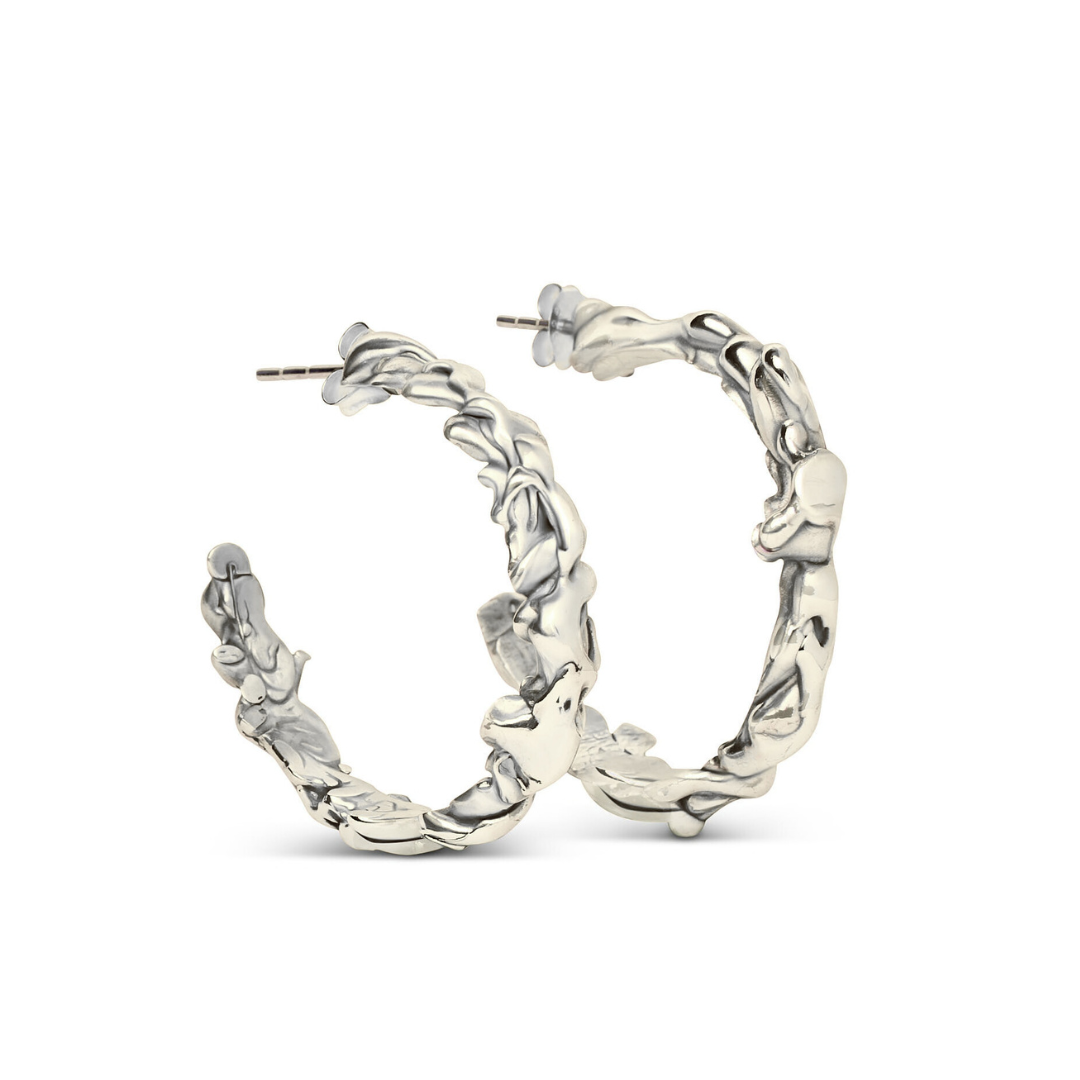 The Molten Hoops Large by Madeleine Sculptural Jewellery are silver hoop earrings with a textured, wavy design, reminiscent of hand-carved pieces, displayed upright against a white background.