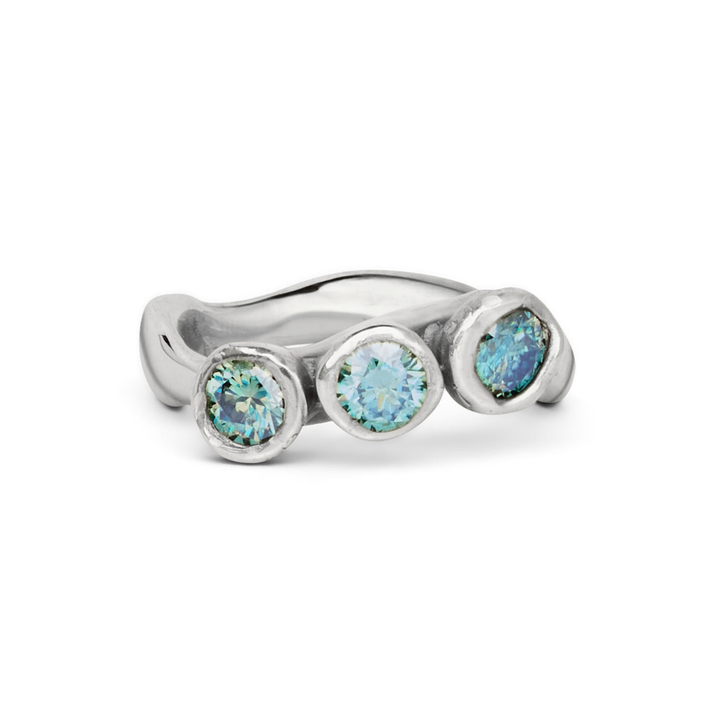 The Moonwater Ring by Madeleine Sculptural Jewellery is a silver moissanite ring with three round, blue-green bezel-set stones and a wavy, modern band—a stunning piece of sustainable jewellery.