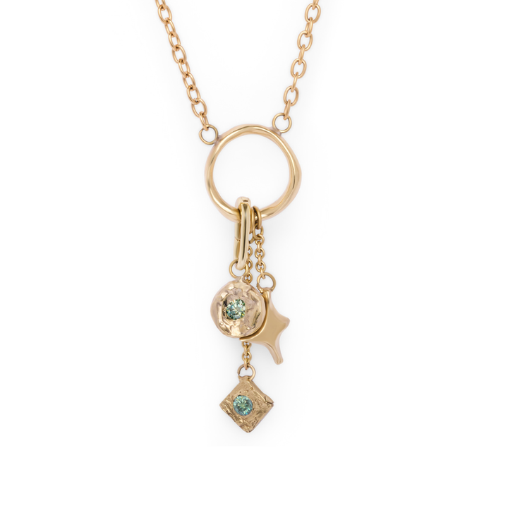 The Spark Necklace from Madeleine Sculptural Jewellery features a gold chain with a circular pendant, adorned with three dangling charms: a textured disc set with a green gem, an abstract star shape, and a small square charm accented by a green stone. Displayed against a white background.