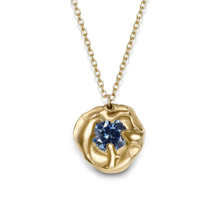 The Molten Necklace with Moissanite by Madeleine Sculptural Jewellery features a handmade gold pendant with an organic, round shape and a central blue moissanite, suspended from a fine gold chain.
