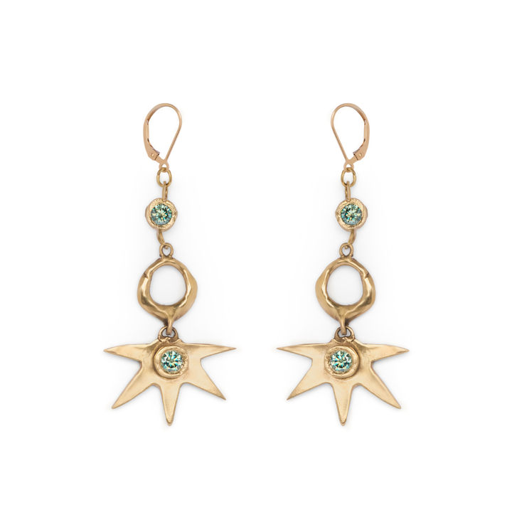 Discover the Réalta Earrings with 2 moissanite by Madeleine Sculptural Jewellery—gold dangle earrings featuring a radiant sunburst motif accented with blue-green gemstones. Each earring showcases a three-part arrangement of circular and star-shaped charms, delicately linked by gold rings. Subtle moon and star accents infuse these earrings with celestial elegance.