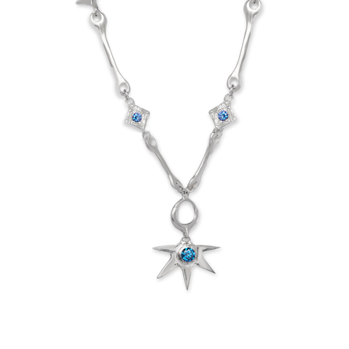 A silver “Bone Necklace with Star Centre” by Madeleine Sculptural Jewellery, adorned with blue gemstones and featuring star-shaped and diamond-shaped pendants, including a central blue gem set in an eight-pointed star.