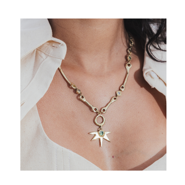 A person wearing a cream-colored shirt showcases the Madeleine Sculptural Jewellery Bone Necklace with Star Centre, featuring a distinctive chain and a large star-shaped pendant adorned with a central gemstone.