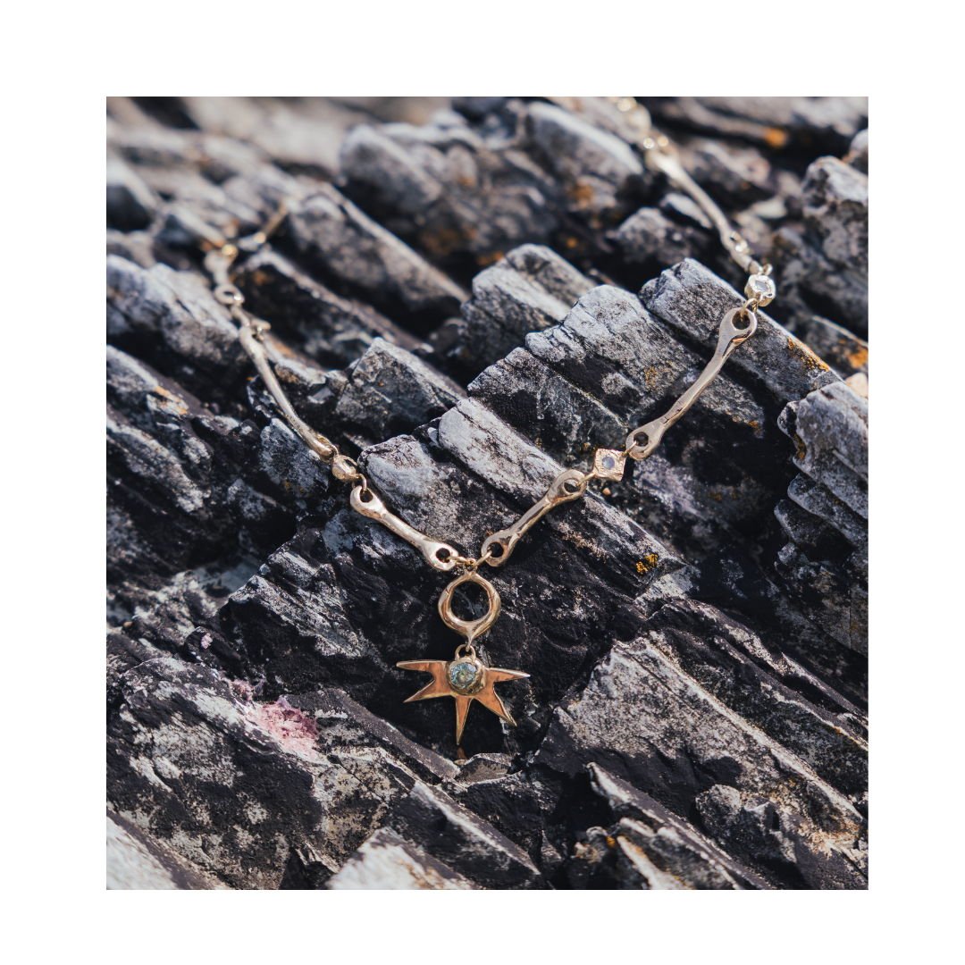 A Bone Necklace with Star Centre from Madeleine Sculptural Jewellery rests on textured gray rocks.