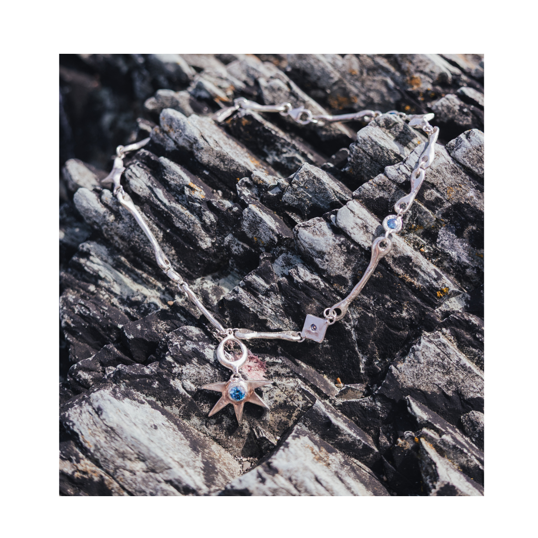 A Bone Necklace with Star Centre by Madeleine Sculptural Jewellery, featuring a striking star-shaped pendant, is displayed atop gray, textured rocks.