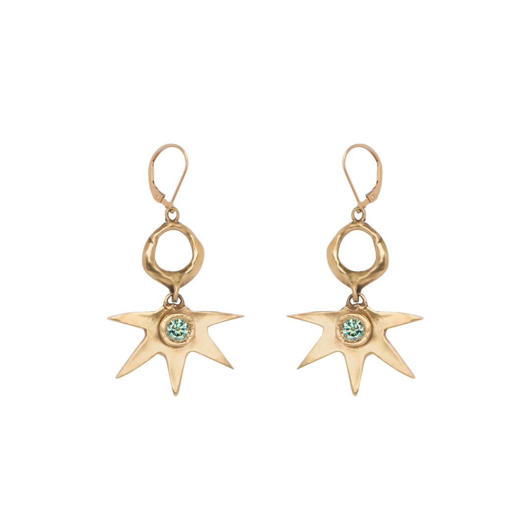 The Realta Earrings with 1 Moissanite by Madeleine Sculptural Jewellery are a pair of gold dangle earrings featuring irregular star-shaped pendants, each set with a small green gemstone at the center and finished with lever-back clasps.