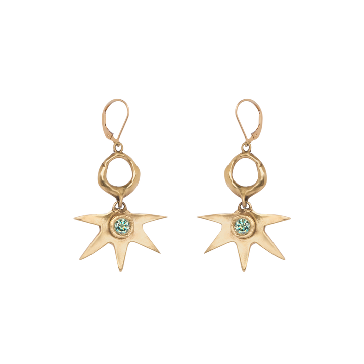 The Realta Earrings with 1 Moissanite by Madeleine Sculptural Jewellery are a pair of gold dangle earrings featuring irregular star-shaped pendants, each set with a small green gemstone at the center and finished with lever-back clasps.