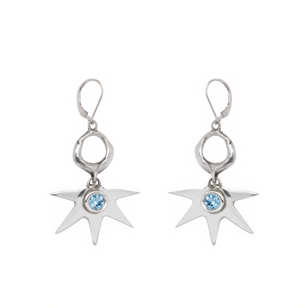 Madeleine Sculptural Jewellery’s Realta Earrings with 1 Moissanite feature silver, star-shaped drops with eight pointed rays radiating from a striking blue gemstone at the center and are finished with lever-back closures.