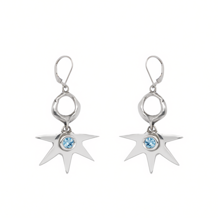 Madeleine Sculptural Jewellery’s Realta Earrings with 1 Moissanite feature silver, star-shaped drops with eight pointed rays radiating from a striking blue gemstone at the center and are finished with lever-back closures.
