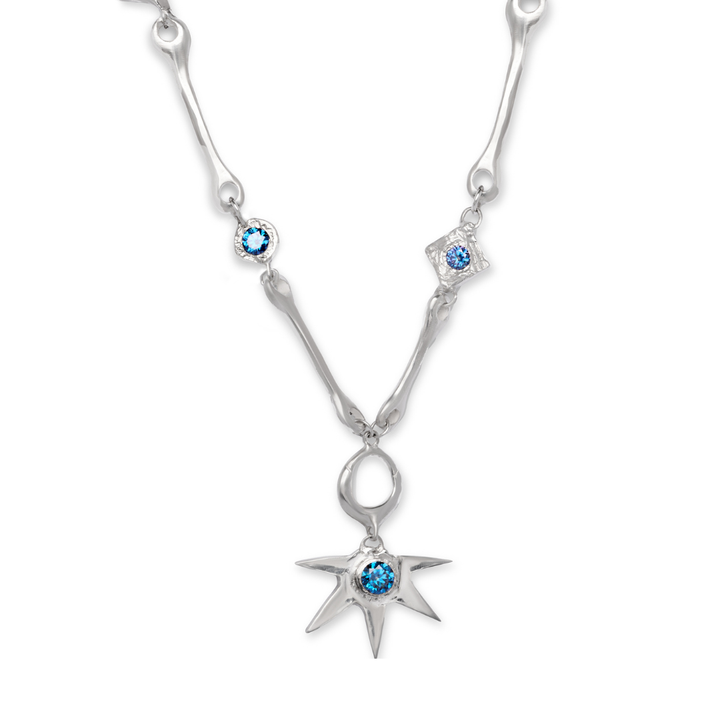 The Réalta Necklace with Moissanite by Madeleine Blaine features a silver chain adorned with blue gemstones, showcasing a star-shaped pendant and two smaller gemstone accents along the chain, set against a white background.