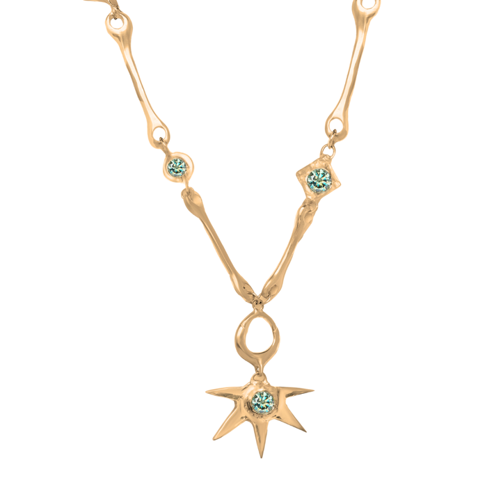 Discover the Réalta Necklace with Moissanite by Madeleine Blaine, featuring an organic, branch-inspired gold chain adorned with light blue gemstones. The pendant showcases a spiked star design centered with a luminous blue Moissanite gem, elegantly suspended from a loop.