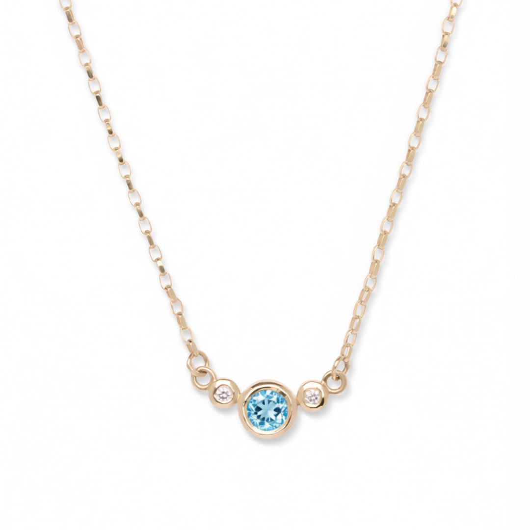 Introducing the Azure Embrace 9ct Yellow Gold Necklace with Two Diamonds from Madeleine Fine Jewellery. This elegant gold chain necklace showcases a central round blue topaz gemstone embraced by two sparkling lab grown diamonds, each set in luxurious gold bezels. Photographed against a plain white background, this sophisticated piece beautifully blends modern refinement with timeless appeal.