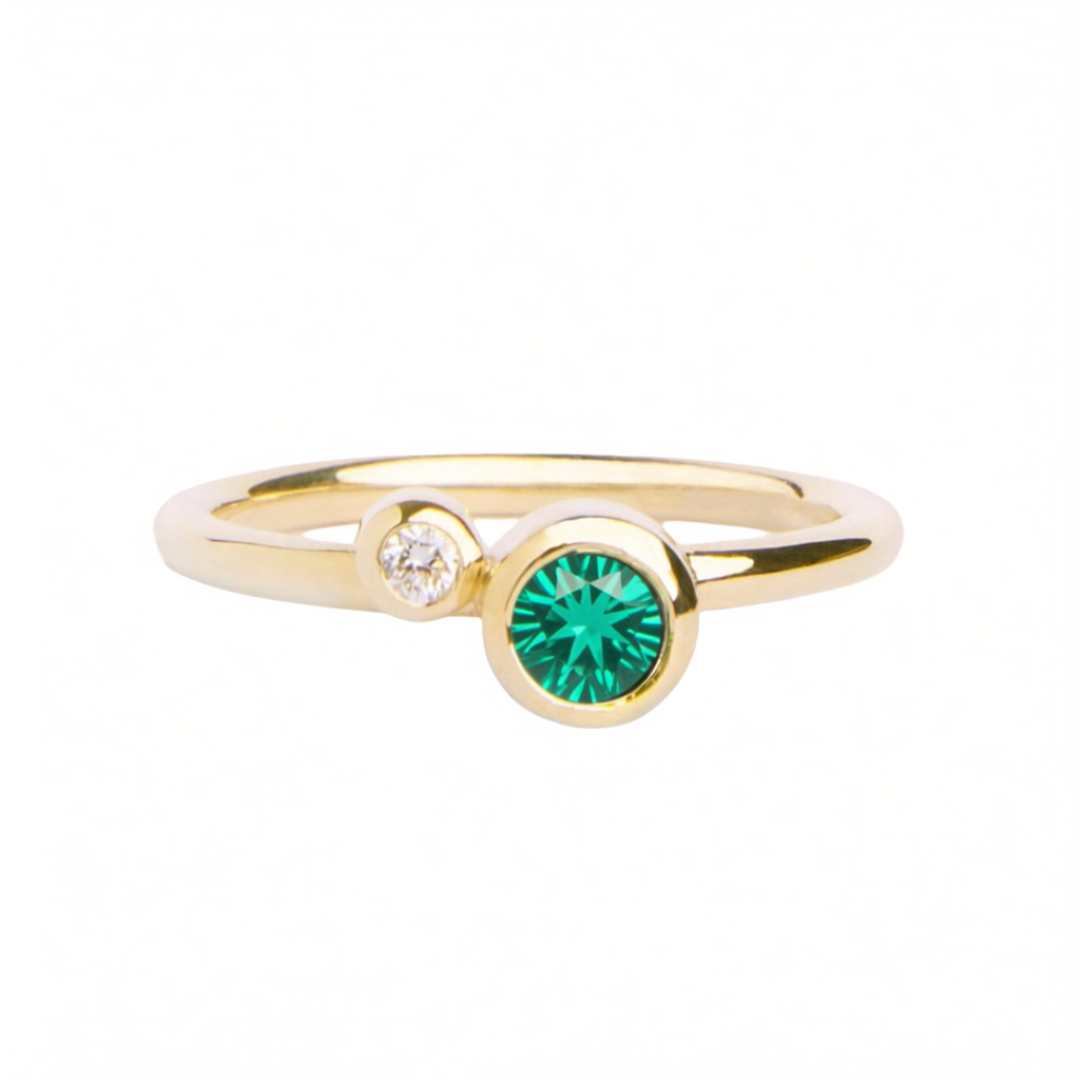 The Willow Shimmer 9ct yellow gold ring with Green Tsavorite & Diamond by Madeleine Fine Jewellery features a small round white diamond set beside a larger round green tsavorite gemstone on a delicate yellow gold band, beautifully showcased against a white background.