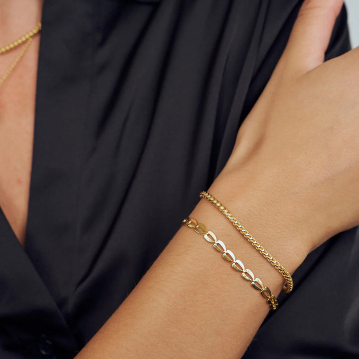 A person in a black shirt wears two bracelets: one with an interlocking leaf design and the other, the Sif Jacobs Muro Bracelet Silver—a simple chain—elegantly crossed over their body to showcase chic demi-fine jewellery.