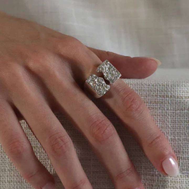 A hand with a natural manicure rests on textured fabric, wearing the Majesty Ring by Inó Jewellery—a handcrafted raw silver signet featuring two rectangular, diamond-encrusted segments facing each other.
