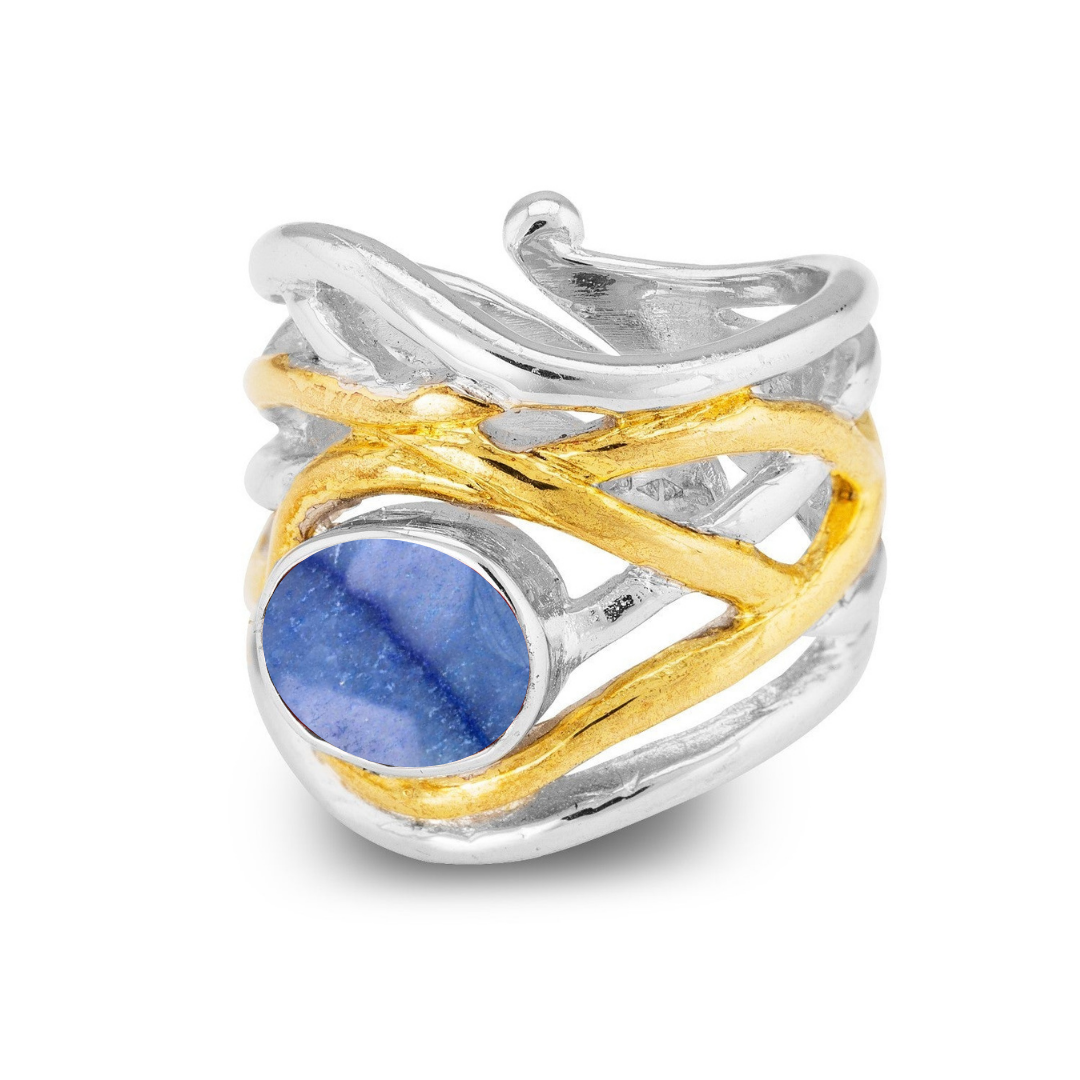 The Adjustable Mayhem Ring from Gallardo & Blaine Designs features a wide, wavy band with intertwining silver and gold tones, highlighted by a bezel-set, prominent round blue gemstone in a medieval-inspired swirl design.