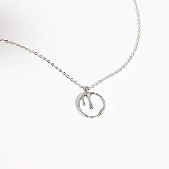 A sterling silver necklace with a delicate chain featuring a round pendant. The pendant has an abstract, wavy line design in the center, creating a minimalist and elegant appearance. Adding to its charm, the background showcases shimmering abalone shell patterns against plain white. Introducing the Melting Pendant Necklace Silver by Marie June Jewellery.