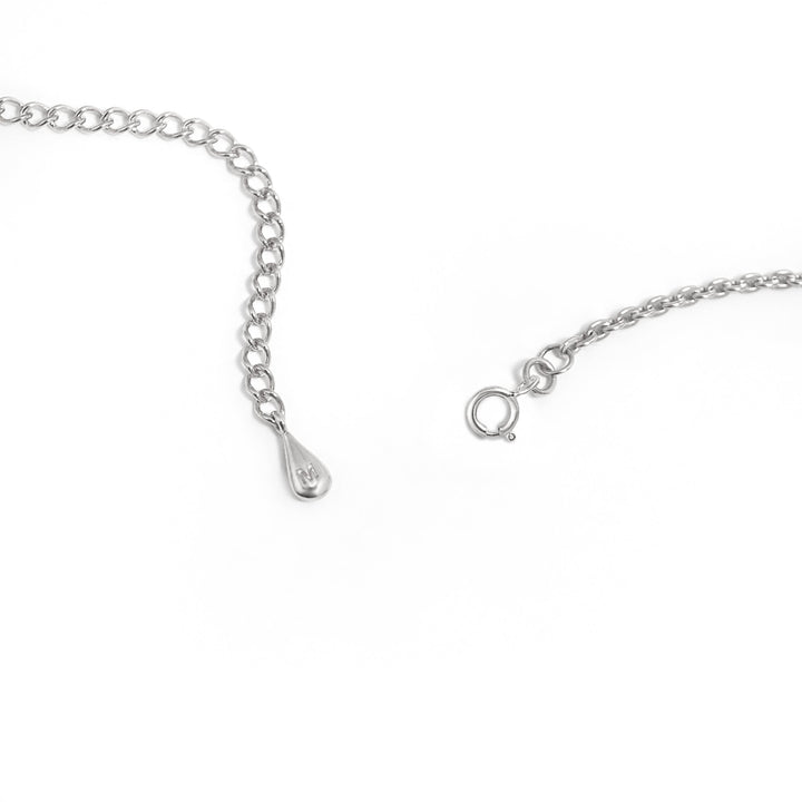 A close-up photo of the ends of a Melting Pendant Necklace Silver by Marie June Jewellery on a white background. One end features a small teardrop-shaped charm, while the other end has a spring ring clasp for fastening. The charm is elegantly inlaid with mother of pearl, adding a touch of sophistication.