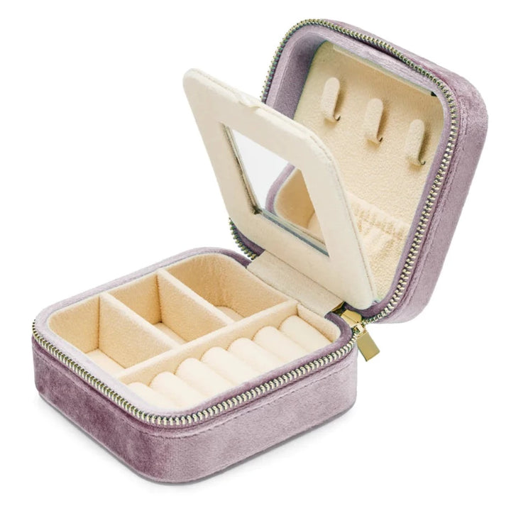 The SoCases Luxurious Metallic Lilac Velvet Travel Jewellery Box is a compact, velvet-covered lavender-colored jewelry box with a zipper, opened to reveal a soft cream interior. It has compartments for rings, earrings, and other jewelry, with slots for rings, three divided sections, and hooks on the inside of the lid.