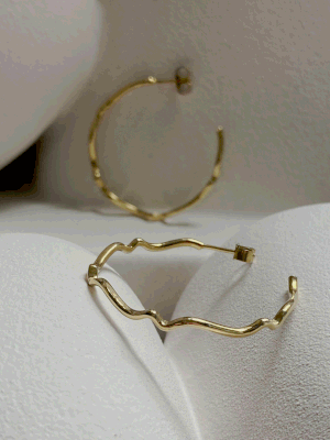 The Sister Hoops by Inner Island, gold wavy hoop earrings shown on a textured white surface—one flat, one upright—are stylish and versatile accessories for jewellery lovers.