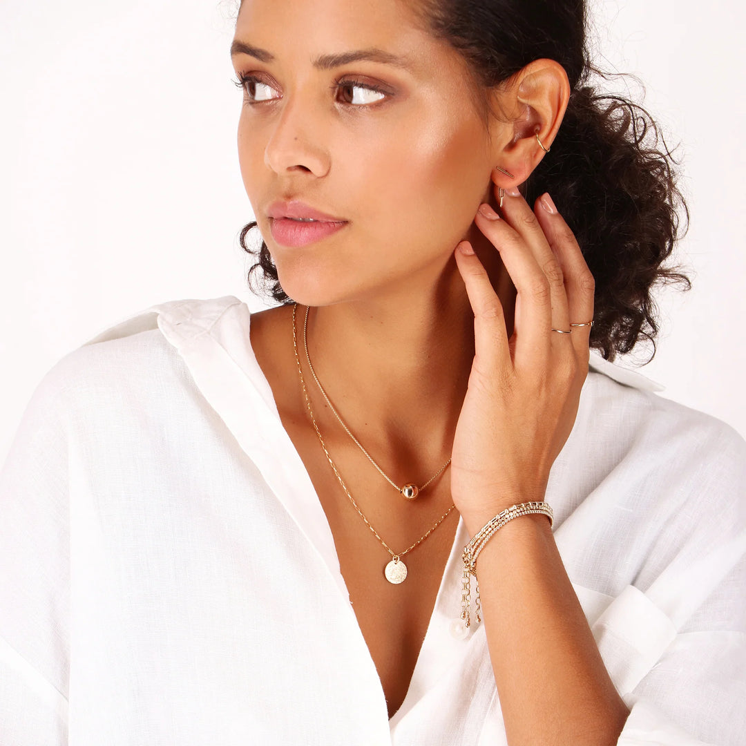 Woman wearing gold jewelry including a necklace, bracelet, and earrings on a white background