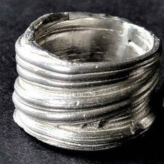 A close-up image of a Mitsuro Silver Ring by Abbie Dixon that appears to be 3D-printed with a rough, layered texture. The Sterling Silver ring has an uneven and unfinished look, showcasing the layers created by the 3D printing process. The background is a dark surface.