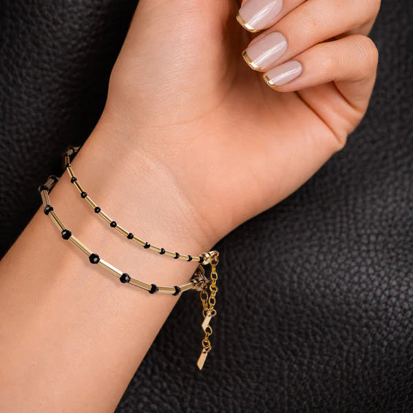 Gold bracelet with black beads on a wrist against a dark background