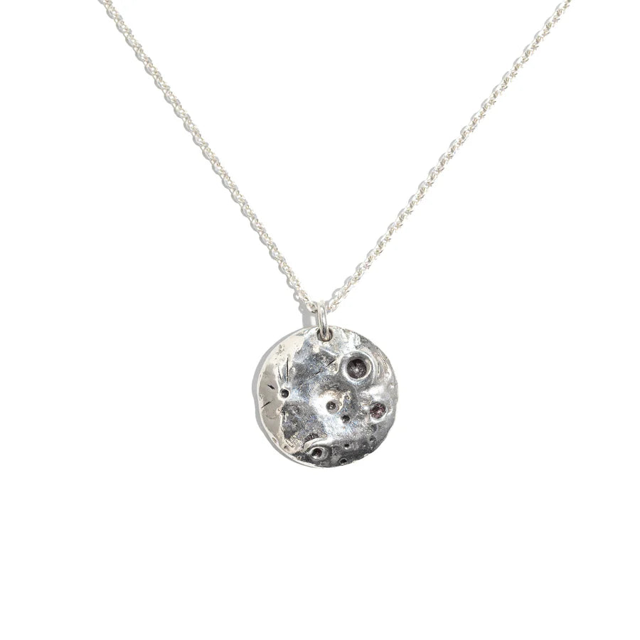 The Pale Raven Molten Moon Silver Necklace showcases a sterling silver, crater-textured pendant—handmade in Dublin—suspended from a delicate chain and displayed against a white background.