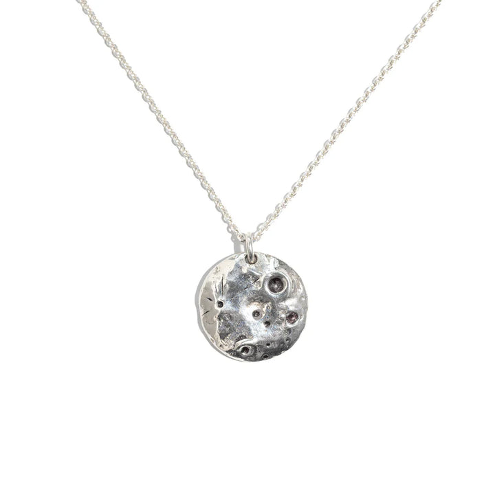 The Pale Raven Molten Moon Silver Necklace showcases a sterling silver, crater-textured pendant—handmade in Dublin—suspended from a delicate chain and displayed against a white background.