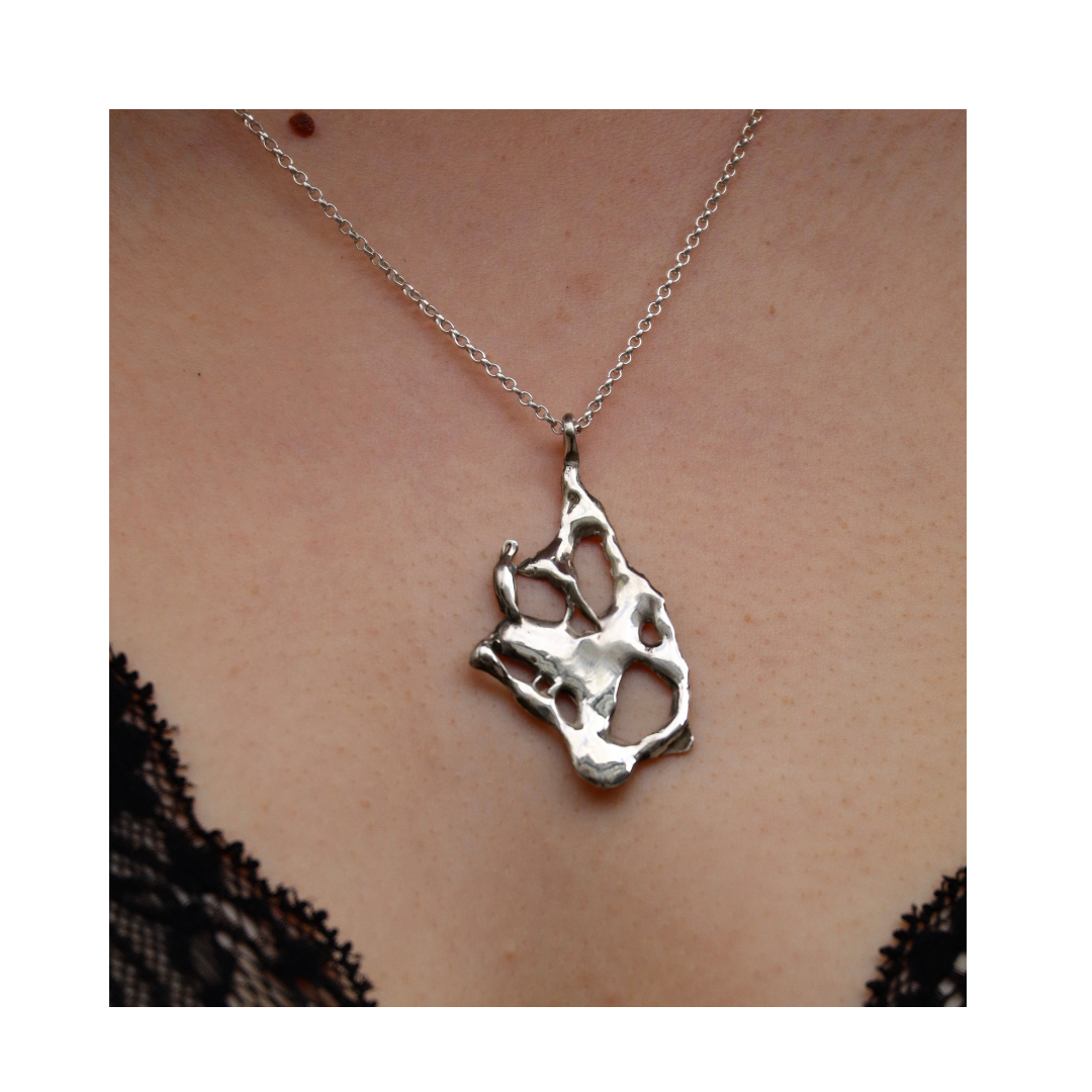 A close-up of a person wearing the Molten Necklace by Madeleine Sculptural Jewellery, featuring organic silver lines on a chain against bare skin, with black lace visible at the edges.
