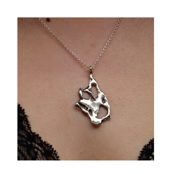 A close-up of a person wearing the Molten Necklace by Madeleine Sculptural Jewellery, featuring organic silver lines on a chain against bare skin, with black lace visible at the edges.