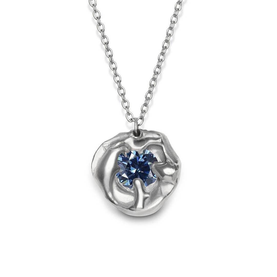 The Molten Necklace with Moissanite by Madeleine Sculptural Jewellery features a hand-carved silver pendant with an abstract organic design and a brilliant blue moissanite centerpiece, suspended from a silver chain.