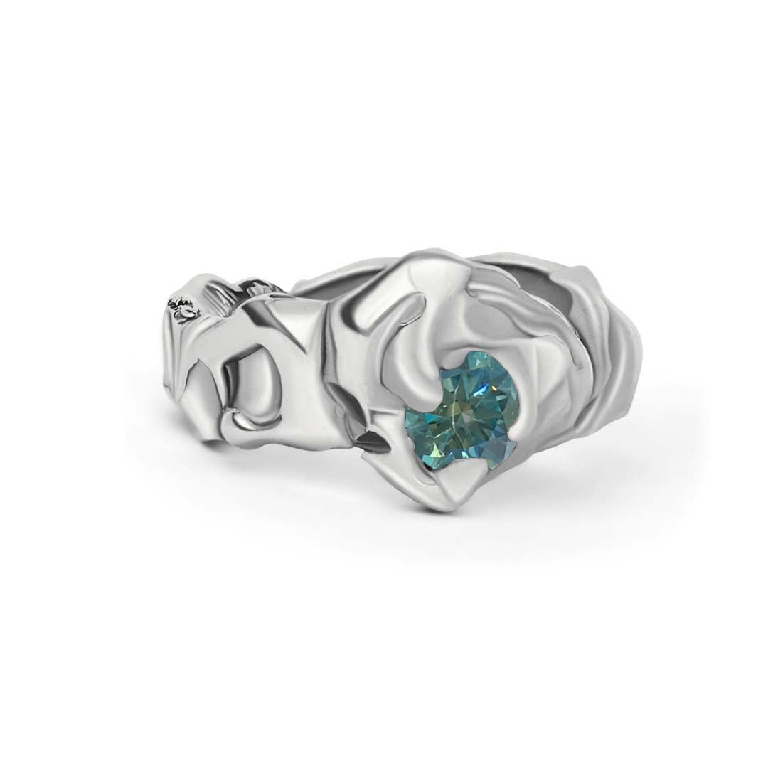 The Molten Ring with Moissanite by Madeleine Sculptural Jewellery is a silver ring featuring a sculpted, folded-metal design and a round blue-green moissanite gemstone set at its center.