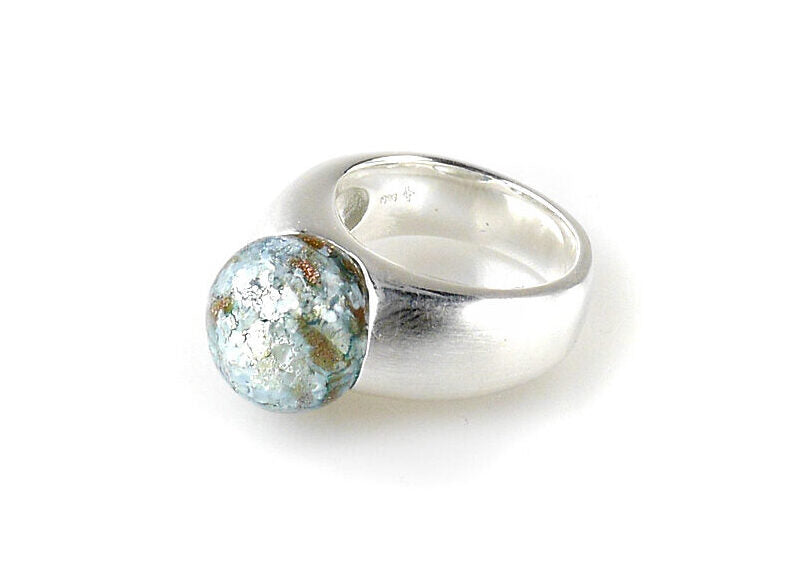 A chunky, handcrafted sterling silver ring featuring a large, round, textured Murano Glass Perle with a mix of Curacao Denim Blue, white, and brown hues. The band is thick and shiny, with the gemstone prominently set on top. The Detlef Menard Muranoperle Silver Ring 12mm has a modern and artistic design.