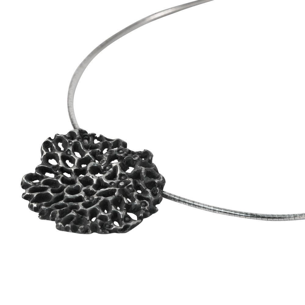 A close-up image of a silver choker necklace featuring a unique, black, coral-shaped pendant. The oxidised sterling silver pendant exhibits an intricate, porous design, resembling natural coral formations. The modern sculptural jewelry has a sleek appearance with a simple, elegant chain.

Product Name: Mythology Large Pendant Oxidised
Brand Name: Abbie Dixon