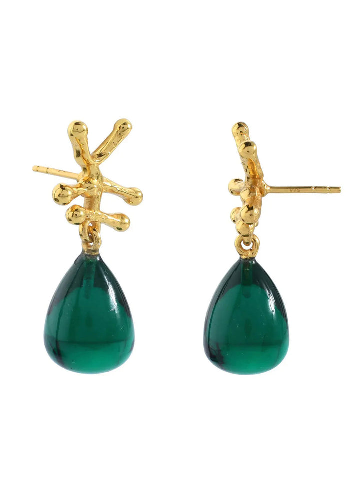 Introducing the stunning Nuria Earrings by Shyla: a pair of gold-colored drop earrings with a branch-like design at the top, each adorned with a teardrop-shaped green gemstone pendant hanging below. Perfectly complemented by raw smoky crystal accents, these earrings exude an elegant charm.