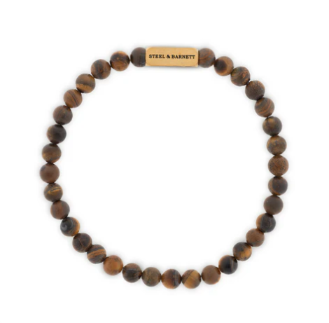 The Steel and Barnett Natural Ned 6mm Round Gemstone Bracelet features matte brown tiger eye beads and a gold stainless steel clasp engraved "STEEL & BARNETT," shown in a circular arrangement on a white background.