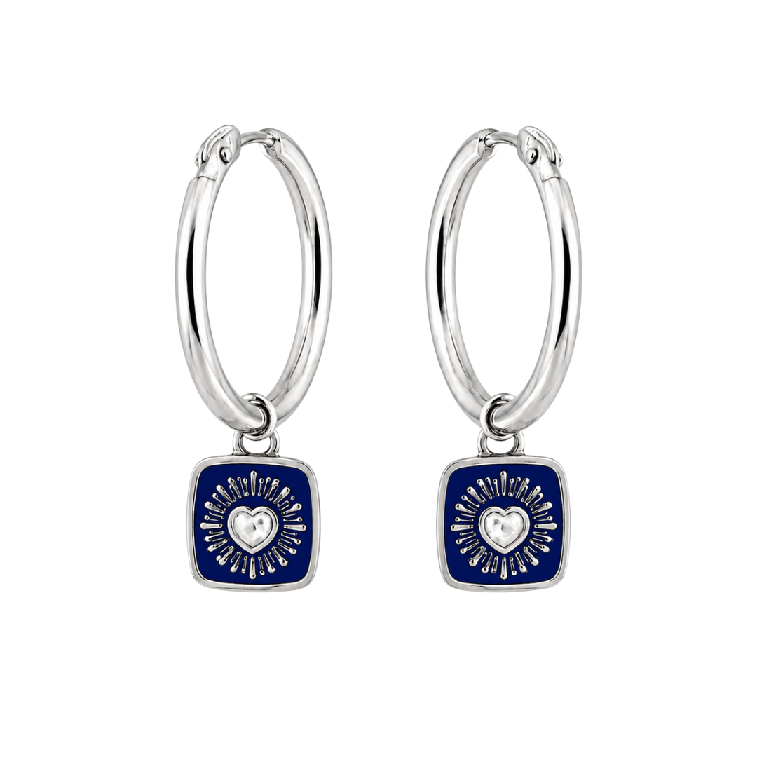 Handmade in Dublin by The Collective Dublin, the Double Sided Keith Haring Claddagh Hoop Earrings are crafted from sterling silver and feature square navy blue charms. Each charm is adorned with a central silver heart surrounded by radiating lines, presenting a modern and elegant design against a white background.