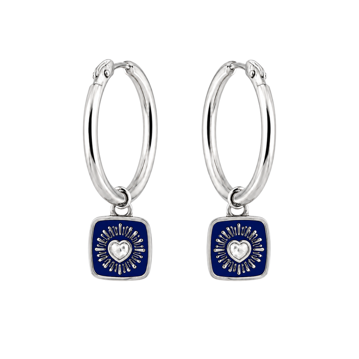 Handmade in Dublin by The Collective Dublin, the Double Sided Keith Haring Claddagh Hoop Earrings are crafted from sterling silver and feature square navy blue charms. Each charm is adorned with a central silver heart surrounded by radiating lines, presenting a modern and elegant design against a white background.