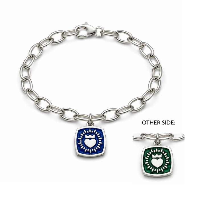 The Double Sided Keith Haring Claddagh On Charm Bracelet by The Collective Dublin is a silver chain bracelet inspired by classic Irish jewelry, featuring a square charm with a white heart and radiant rays. The charm showcases vibrant blue enamel on one side and green enamel on the other, giving a modern twist reminiscent of a sterling silver Claddagh bracelet.