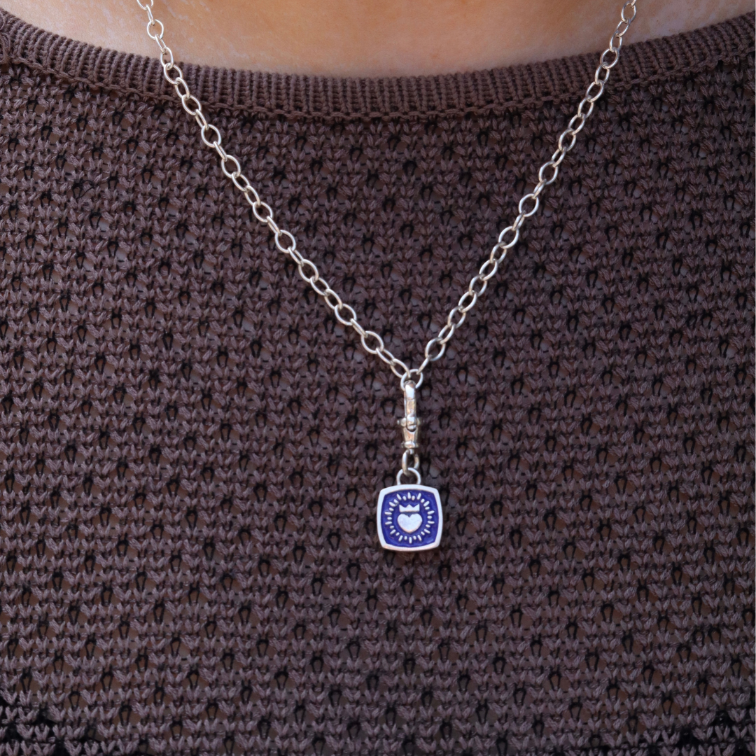 A Double Sided Keith Haring Pendant with Chunky Chain by The Collective Dublin is worn over a textured brown knit top, blending the statement style of contemporary jewelry with a modern twist.