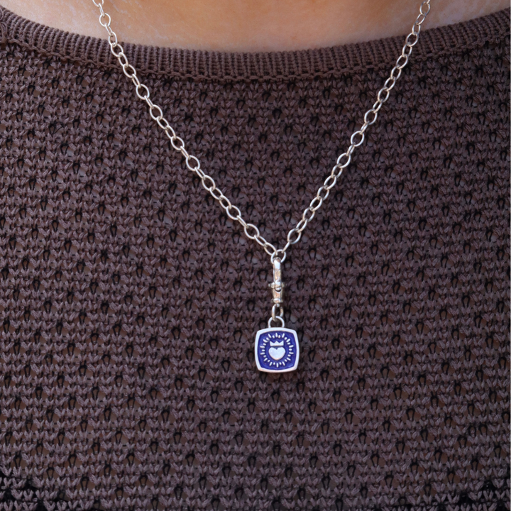 A Double Sided Keith Haring Pendant with Chunky Chain by The Collective Dublin is worn over a textured brown knit top, blending the statement style of contemporary jewelry with a modern twist.