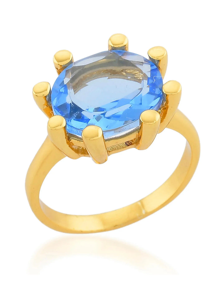 The Shyla Oval Claw Ring in various colours features a chunky gold band with a large oval blue gemstone secured by six claw prongs, shown against a white background.