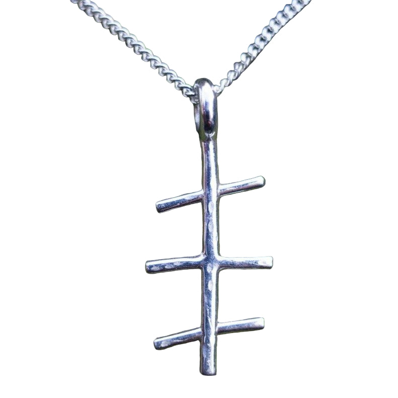 An Ogham Treasure Mam Small Pendant with a unique design resembling a vertical line intersected by three shorter horizontal lines hangs on a sterling silver chain. The background is moss-covered tree bark, creating a natural and rustic setting perfect for showcasing this exceptional Mothers Day gift.