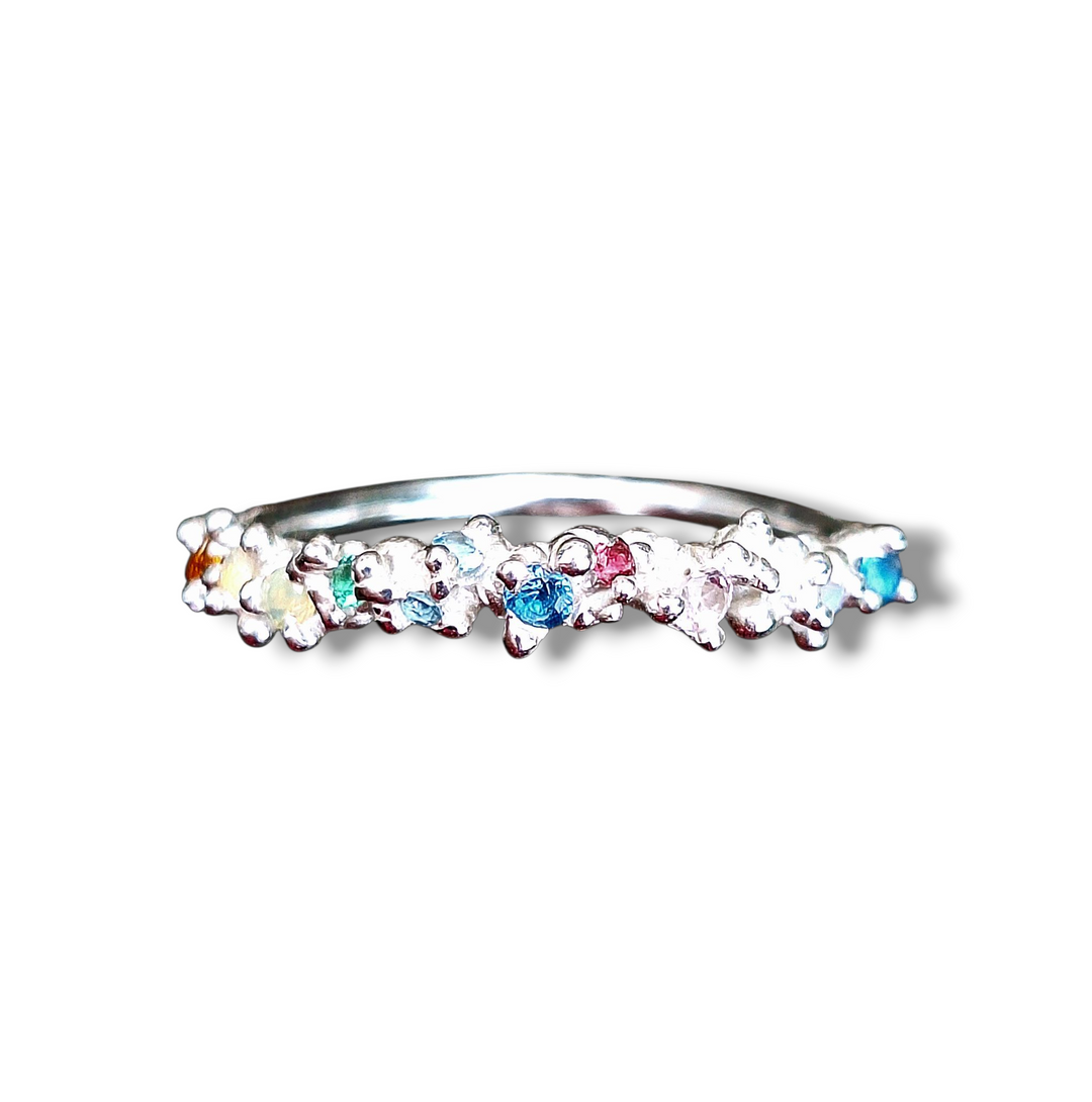 The Pale Raven Starborne Orbit Silver Stacking Ring features lab-grown blue, pink, green, and yellow crystals in a scattered pattern on silver, evoking a relic aesthetic against a white background.