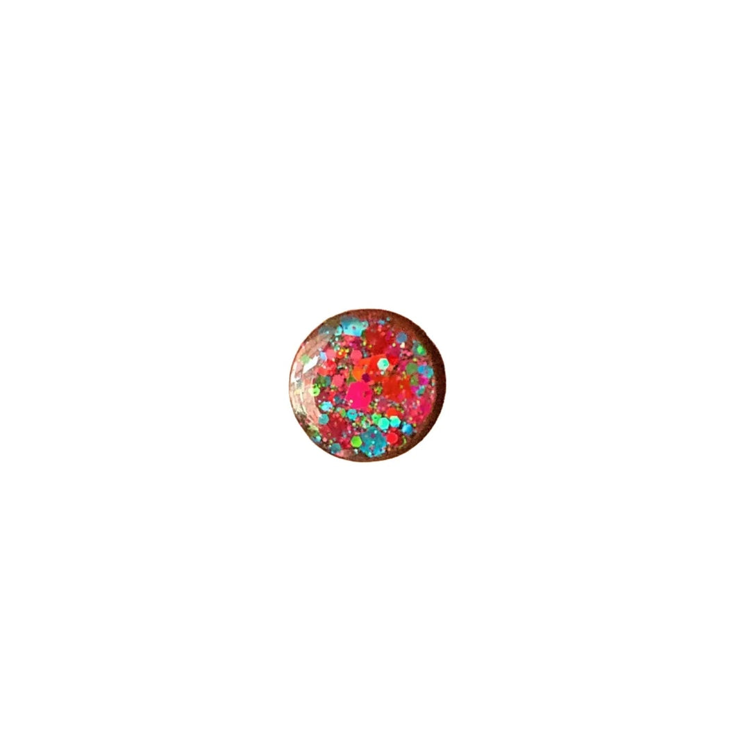 A small, round object with a smooth surface, adorned with a colorful, multicolour glitter pattern. The design includes a mix of red, pink, blue, and green specks, giving it a vibrant and festive appearance against a white background. This is the Party Stud Earrings from Naoi.