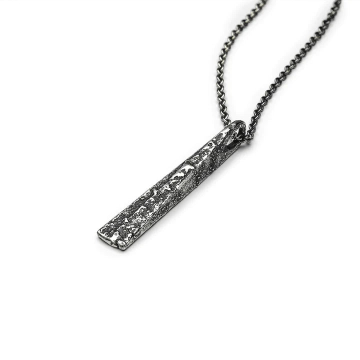 A close-up image of a silver chain necklace featuring a rectangular, textured pendant crafted from patinated 925 silver. This Large Tetrahedron Necklace by Septentrion showcases a rugged, speckled design and hangs from a thin, delicate chain. The white background is unobtrusive, enhancing the intricate details.