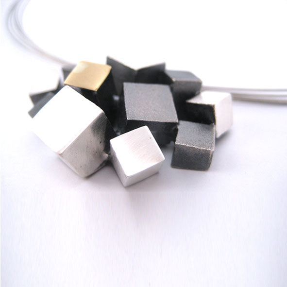 A close-up of the Iceland Pendant from MarCucurella featuring a cluster of metallic cubes in various sizes and finishes, including silver, gold, and dark gray. This piece of handmade jewelry showcases the cubes tightly grouped together in an abstract, three-dimensional design.