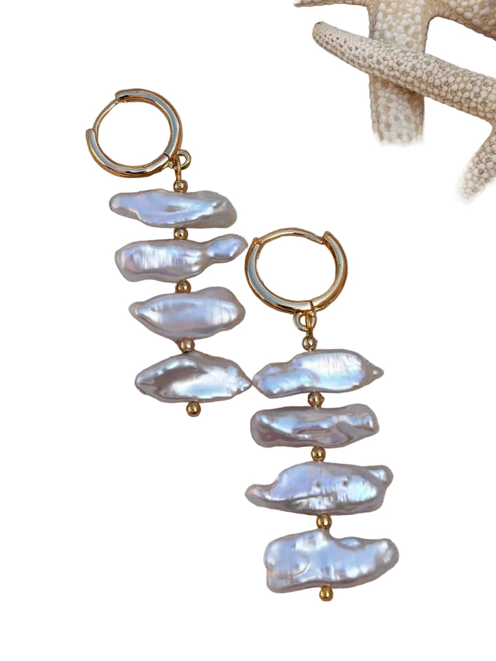 The Perla Sol Earrings by Kybalion Jewellery are gold plated hoops, each featuring three vertically arranged iridescent Biwa pearls, showcased beside a beige starfish on a white background.