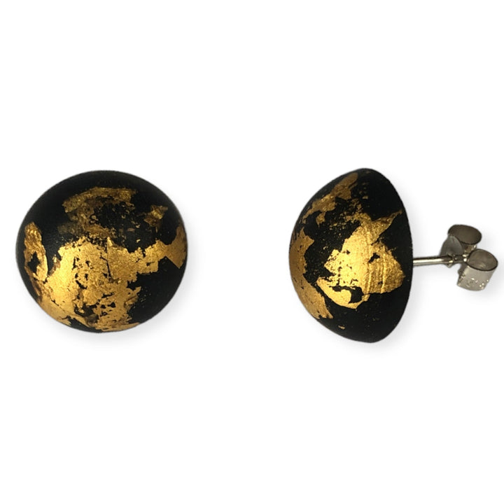 A pair of Angela O'Keefe Luxe Stud Earrings Black with a black base and decorative gold leaf accents. The earrings feature sterling silver posts and butterfly backings. Crafted with resin, the abstract design showcases an uneven yet captivating gold pattern.